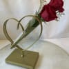 Two red roses in a clear cone vase on a gold heart stand
