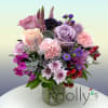 Mixed bouquet of pink and lavender roses, carnations, and purple blooms in a clear glass vase.