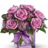 Pink roses in a purple glass vase with a ribbon bow