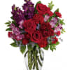 Red roses and purple flowers arranged in a clear glass vase