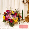 Basket arrangement of mixed flowers beside a green candle