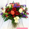 Mixed bouquet of roses, carnations, and purple filler flowers in a glass pitcher vase