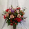 Mixed bouquet of roses, carnations, and purple flowers in a glass vase
