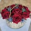 Red roses arranged in a round silver box with blue thistle accents