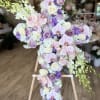 Cross-shaped floral arrangement with pink orchids, white roses, and purple blooms