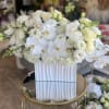 White floral arrangement in a tall ribbed vase with orchids and roses