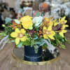 Yellow roses and orchids arranged in a dark vase