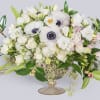 White floral arrangement in a glass compote vase with pink accents