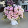 Pink roses arranged in a white pedestal vase with yellow filler flowers
