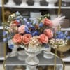Bouquet of peach roses and blue flowers in a white pedestal vase