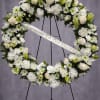 White funeral wreath with roses, lilies, and daisies on a stand