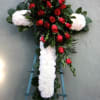 Cross-shaped floral tribute with red roses and white flowers on a stand