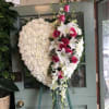Heart-shaped white floral wreath with pink roses and lilies on an easel