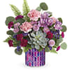 Mixed pink and purple flowers in a patterned vase with a succulent centerpiece