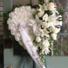 White funeral wreath with lilies and roses and a ribbon reading Loving Mother