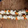 Two white and orange flower garlands laid on a wooden surface