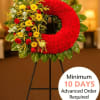 Standing red wreath with yellow and red flowers on one side, displayed on a black easel indoors