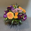 Mixed bouquet of orange, purple, and pink flowers in a glass vase