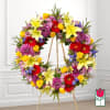 Large floral wreath on a stand with yellow lilies, red gerberas, and purple blooms