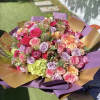 Large hand-tied bouquet of pink, lavender, and peach roses wrapped in purple and gold paper