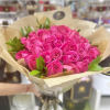Bouquet of bright pink roses wrapped in tan patterned paper with a black ribbon tie.
