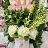 Tall arrangement of pink-tipped roses, white hydrangeas, and green orchids in a white hatbox with pink ribbon