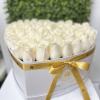 Heart-shaped white box filled with tightly packed ivory roses and tied with a gold satin ribbon.