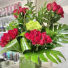 Tall arrangement of red roses with large tropical leaves in a square glass vase