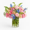A soft, garden-style arrangement in a clear glass vase featuring a blend