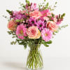 A lush arrangement in a clear glass vase featuring premium roses, gerbera