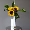 Sunflowers arranged in a tall mirrored vase with curled green leaves
