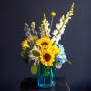 Sunflowers, white snapdragons, and blue hydrangeas in a blue glass vase