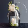 Black lantern with a white candle and cream silk flowers on top