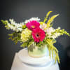 Pink gerbera daisies and white flowers arranged in a pale green vase