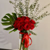 Red roses in a tall glass vase with eucalyptus and a red ribbon