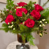 Red roses arranged in a glass vase with evergreen and white berries