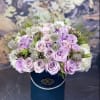 Lavender roses and white filler flowers in a blue hatbox