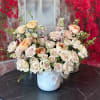 Cream and blush roses arranged in a white vase with a ribbon