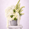Tall white and green floral arrangement with hydrangeas and roses in a gray pot on a pedestal.