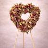 Heart-shaped standing wreath of mauve and yellow flowers on a wooden easel stand