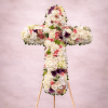 Standing floral cross of white blooms with pink roses and purple accents on a wooden easel