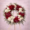 Large standing wreath of red and white flowers with greenery on a wooden easel.