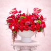 Red rose arrangement in a white pedestal vase with pink anthuriums