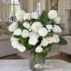 White roses and ranunculus in a glass vase with green leaves