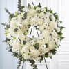 A large circular standing wreath of white roses, lilies, chrysanthemums and small
