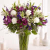 Tall arrangement of white roses and purple blooms in a clear glass vase