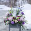 Purple and white floral arrangement in a gray container with an angel figurine