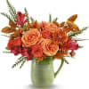 Orange roses and red flowers arranged in a green ceramic pitcher