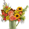 Mixed bouquet of roses, sunflowers, and daisies in a green pitcher vase