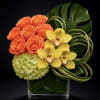 Orange roses, yellow orchids, and green hydrangea in a clear square vase